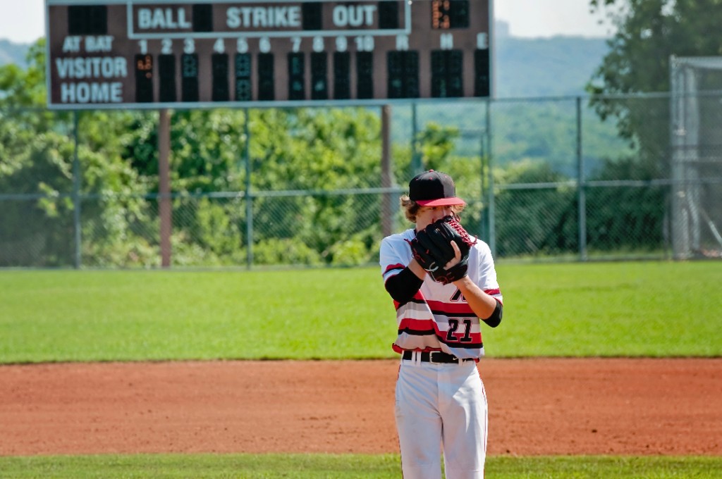 Youth baseball pitcher on the mound in front of a scoreboard