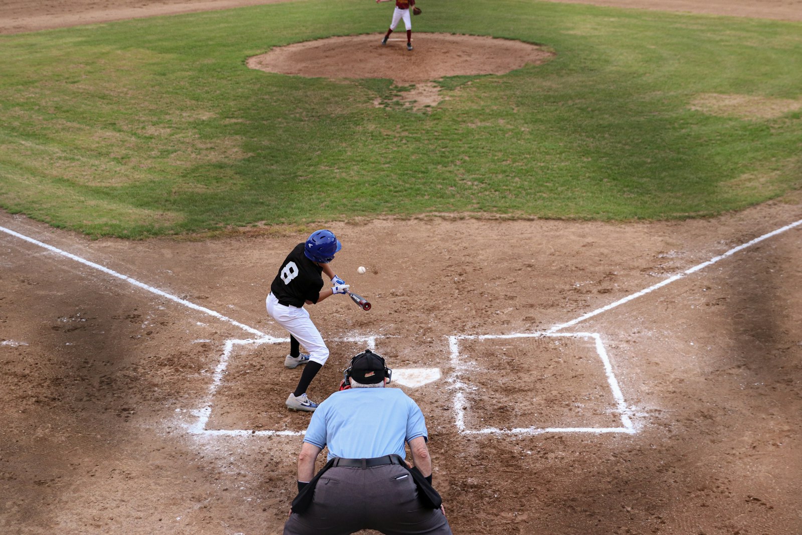 Youth baseball batter swinging at a pitch with the umpire behind the plate