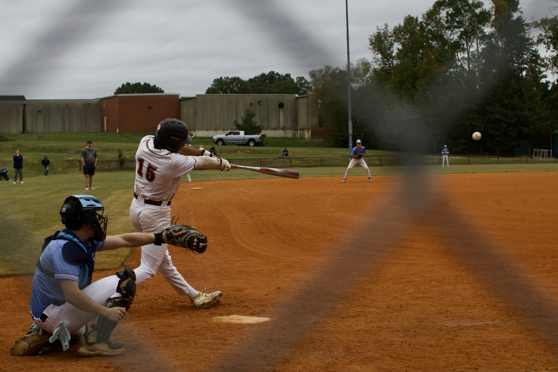Baseball player swinging at a pitch with catcher behind home plate